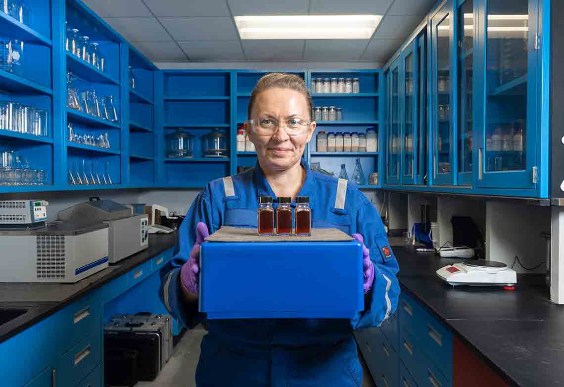 Potograph of woman in blue coveralls in a lab holding samples of solvent (SLBHoustonCarbon00003-Edited)
