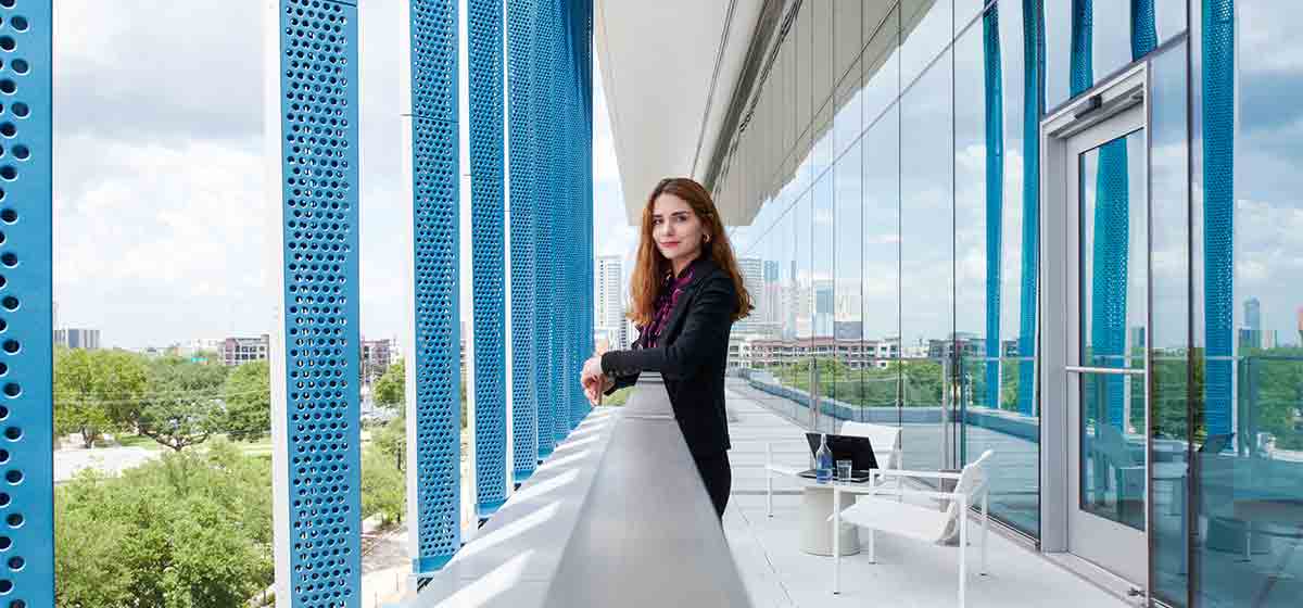 Woman standing on the balcony of a blue and white office building (Tier 1_Office_Houston_AML_4697)