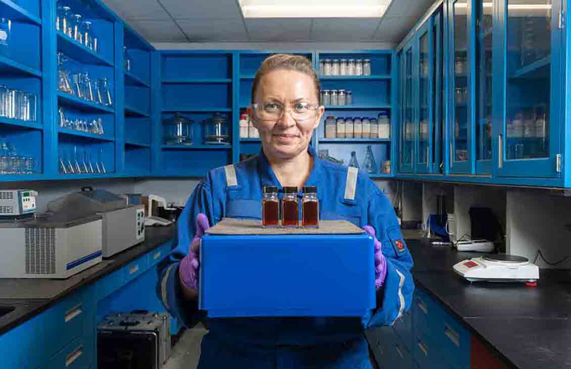Photograph of woman in blue coveralls in a lab holding samples of solvent (SLBHoustonCarbon00003-Edited)
