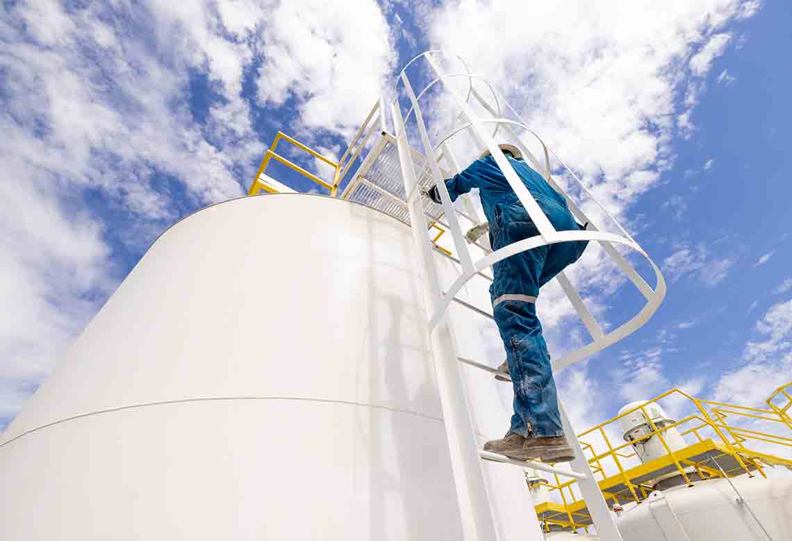 Photo of worker climbing up large tank