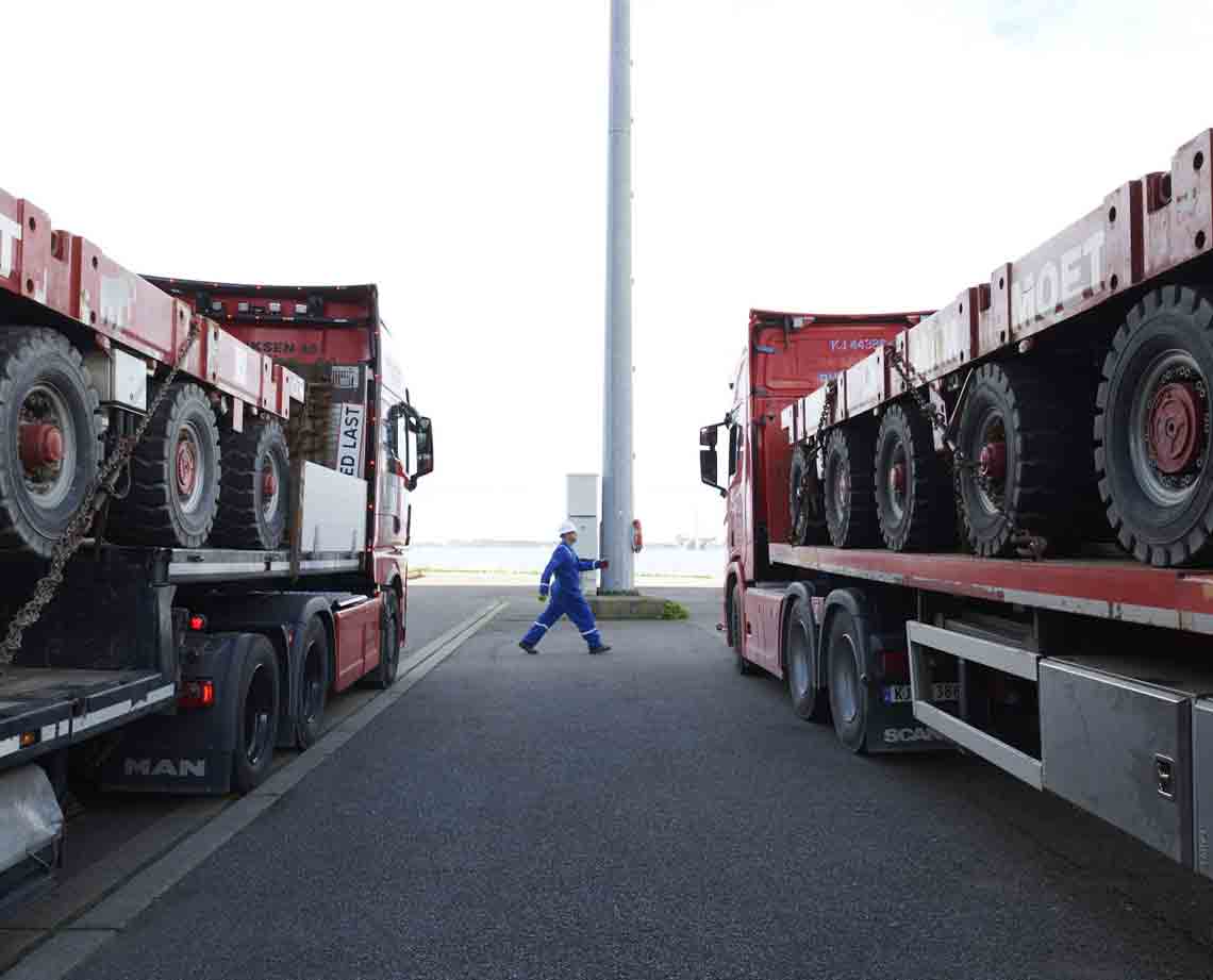 Photo of person walking, large trucks with wheeled platforms on either side 