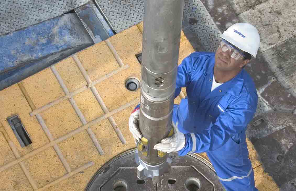 Looking down onto the rig floor where a Schlumberger technician is guiding a PowerV vertical drilling RSS BHA into the hole