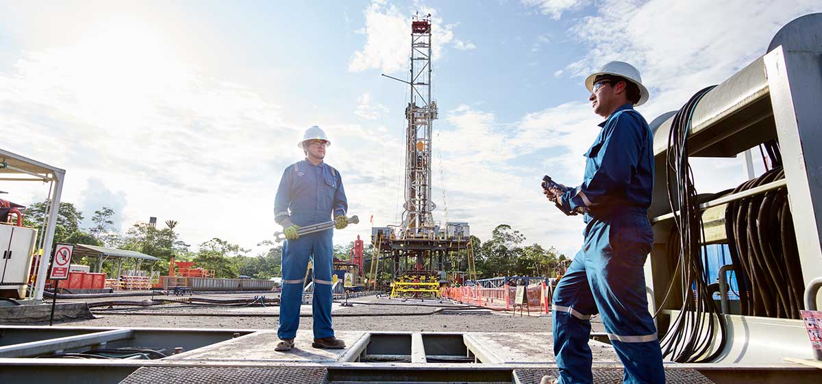 Two SLB operators in front of a drilling land rig