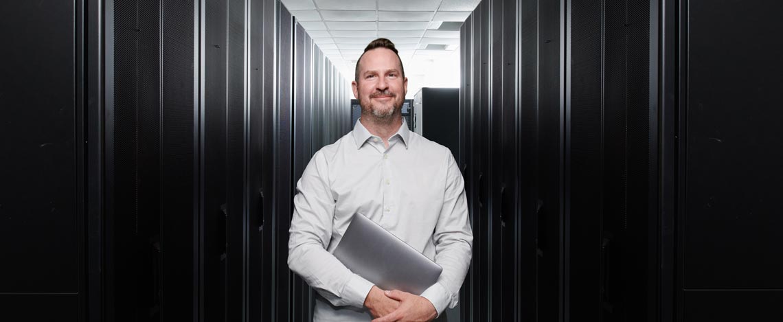 Man holding a laptop in a hallway of servers